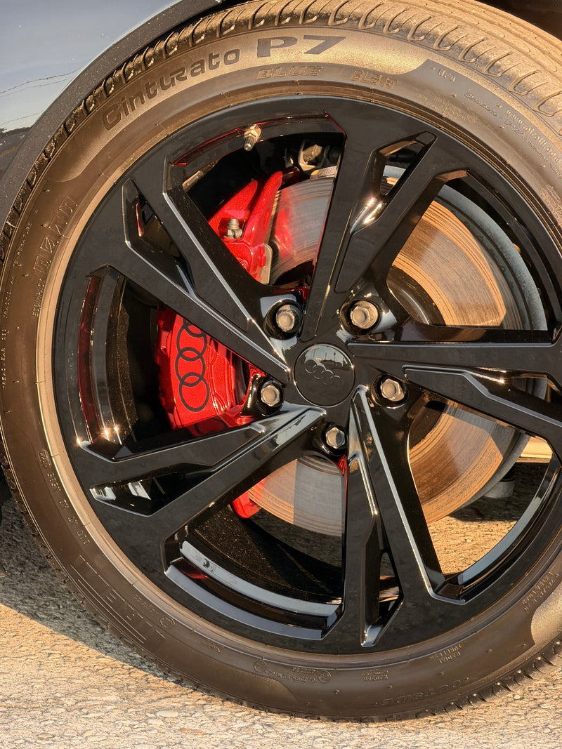 Close-up of a car wheel with black rim and red brake caliper on a road.